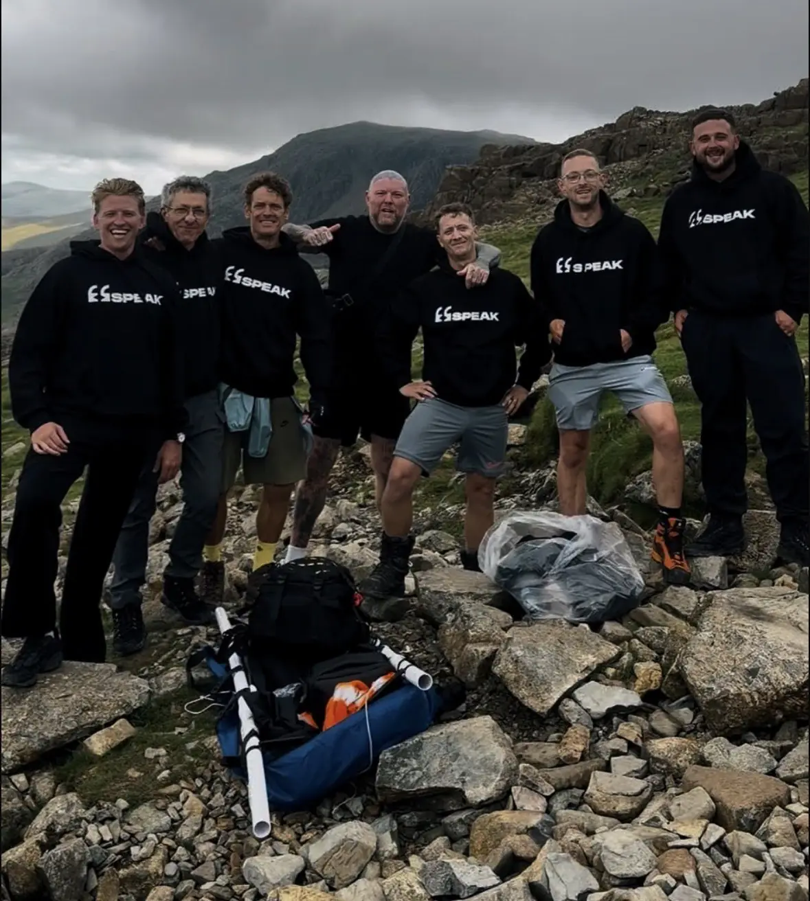 A group of SPEAK members in SPEAK hoodies smiling together on a rocky mountainside